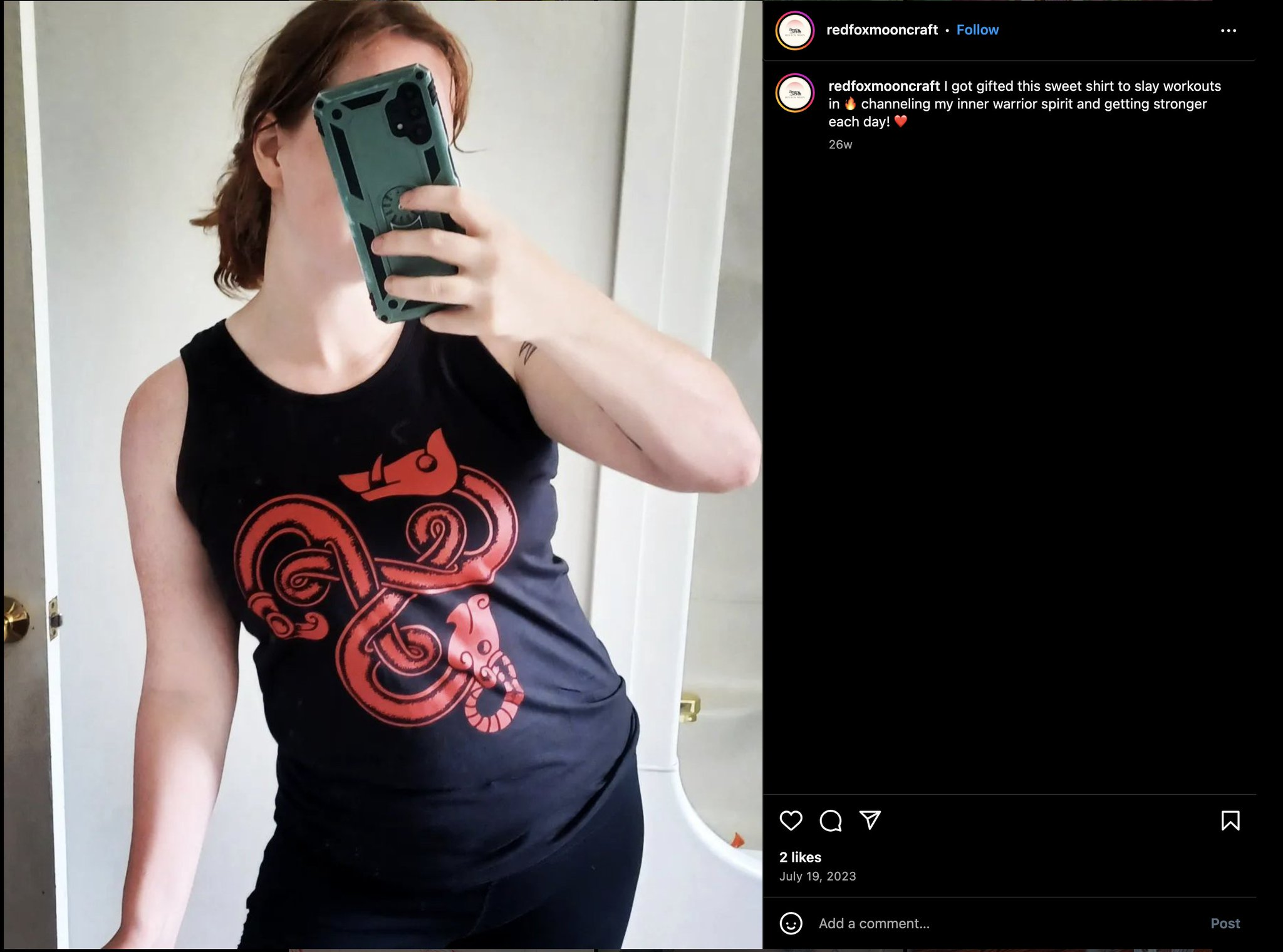Ashley holding her phone over her face taking a picture in the mirror while wearing a Vinland Battlewear shirt.